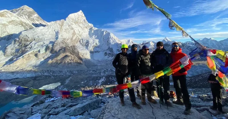 Group of trekkers with Tibetan prayer flags at Kala Patthar summit, the Everest massif filling the sky behind them