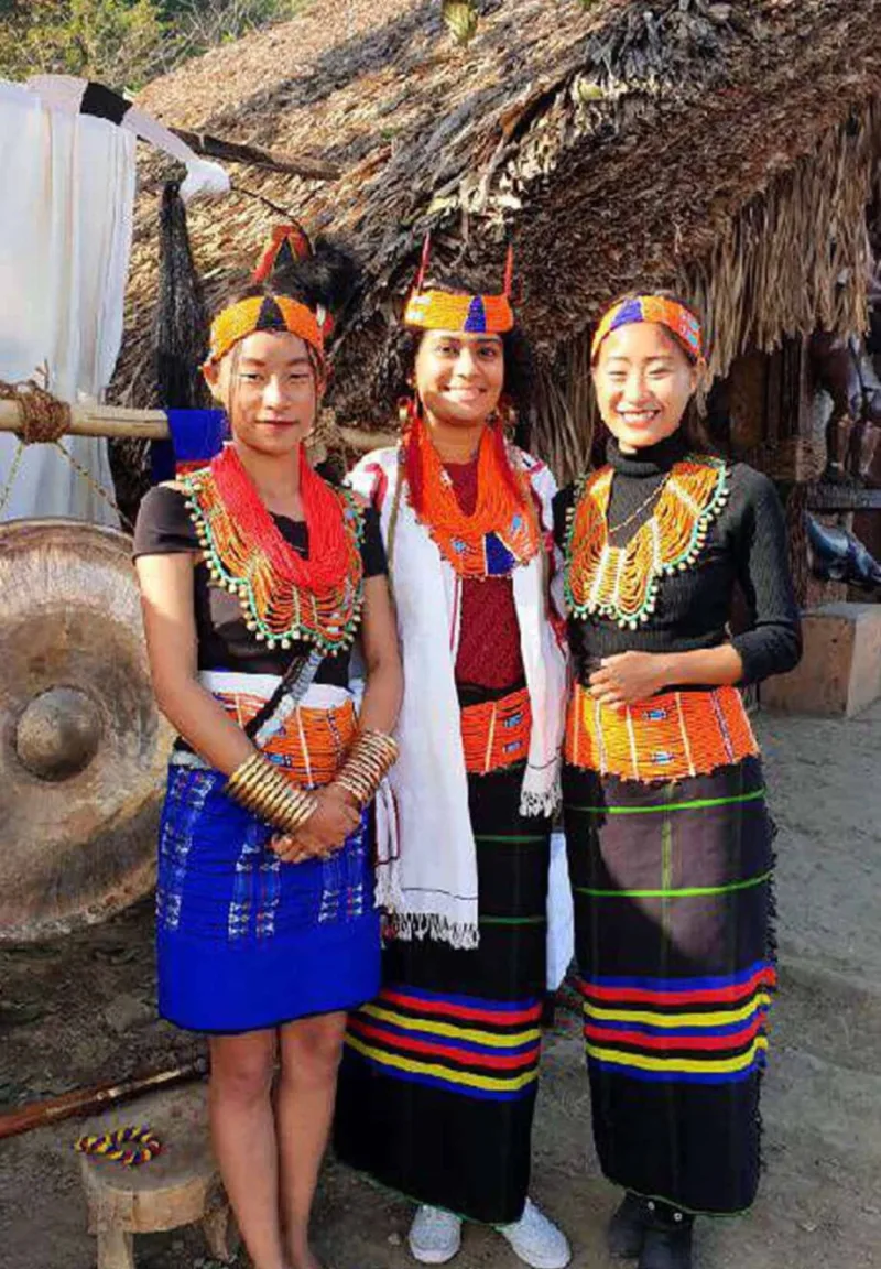 Indian traveller dressed in traditional Naga tribal costume alongside two Naga women in full traditional dress at Kisama Heritage Village