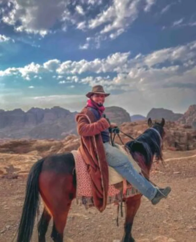 A traveller on horseback in Petra, Jordan, with the rose-red rocky landscape stretching into the distance under a bright sky