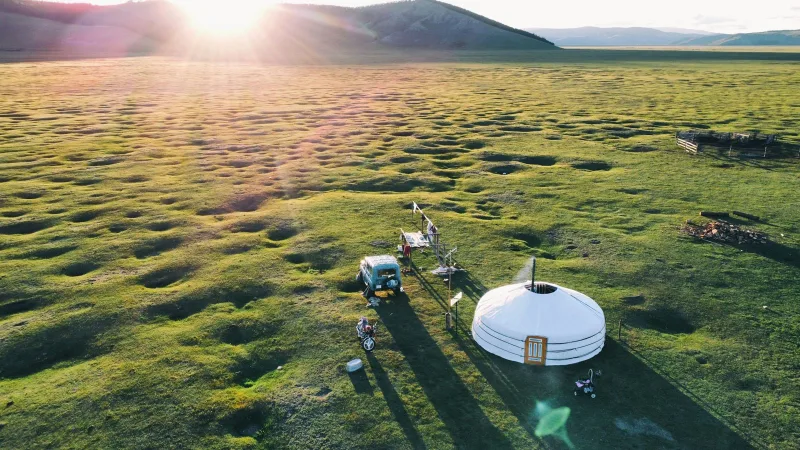 Aerial view of a white ger on the Mongolian steppe at golden hour, hills rising in the background