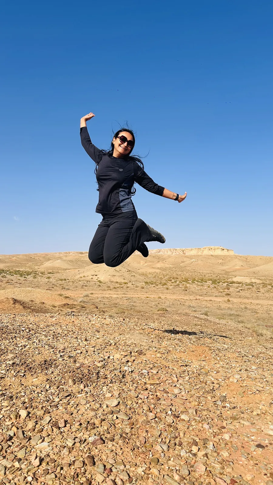 Woman joyfully jumping on the Mongolia group trip with One in the Orange Jacket.