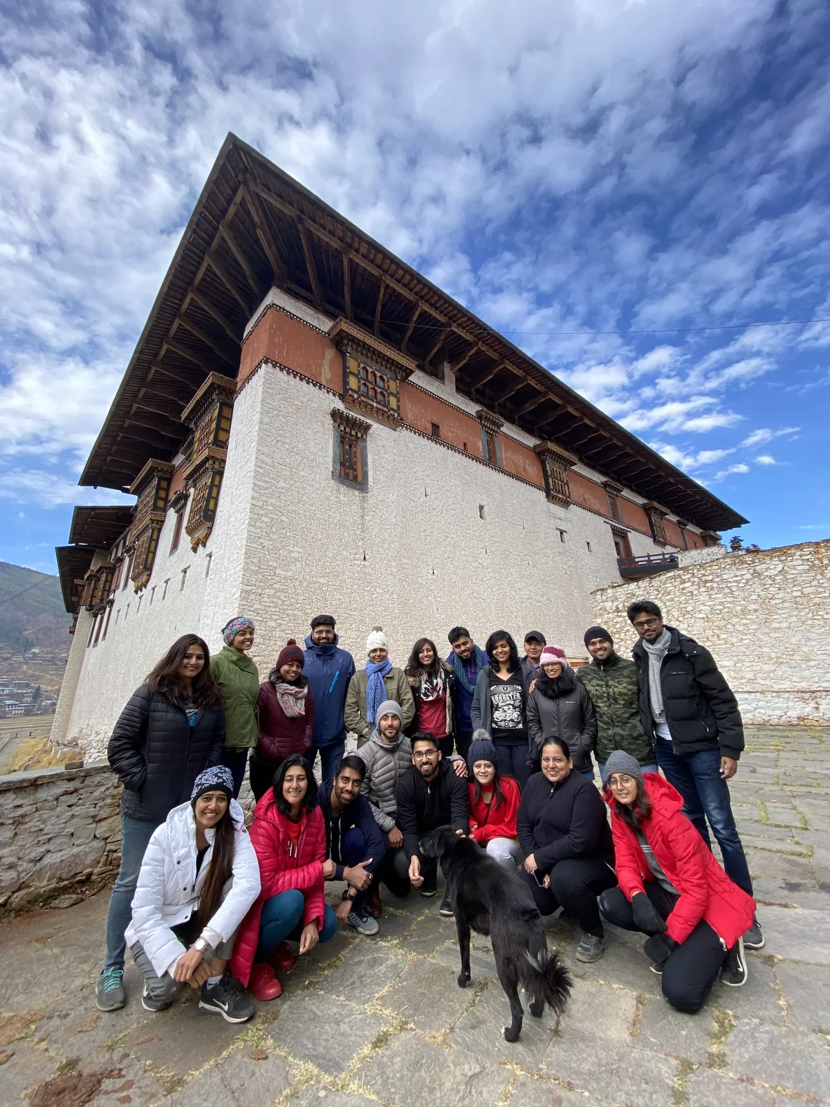 OJ group posing with a dzong dog in front of Paro Dzong under a big sky