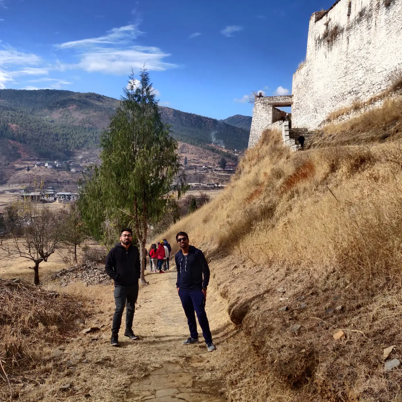Two trippers on the dry winter hillside beneath the Paro Dzong wall