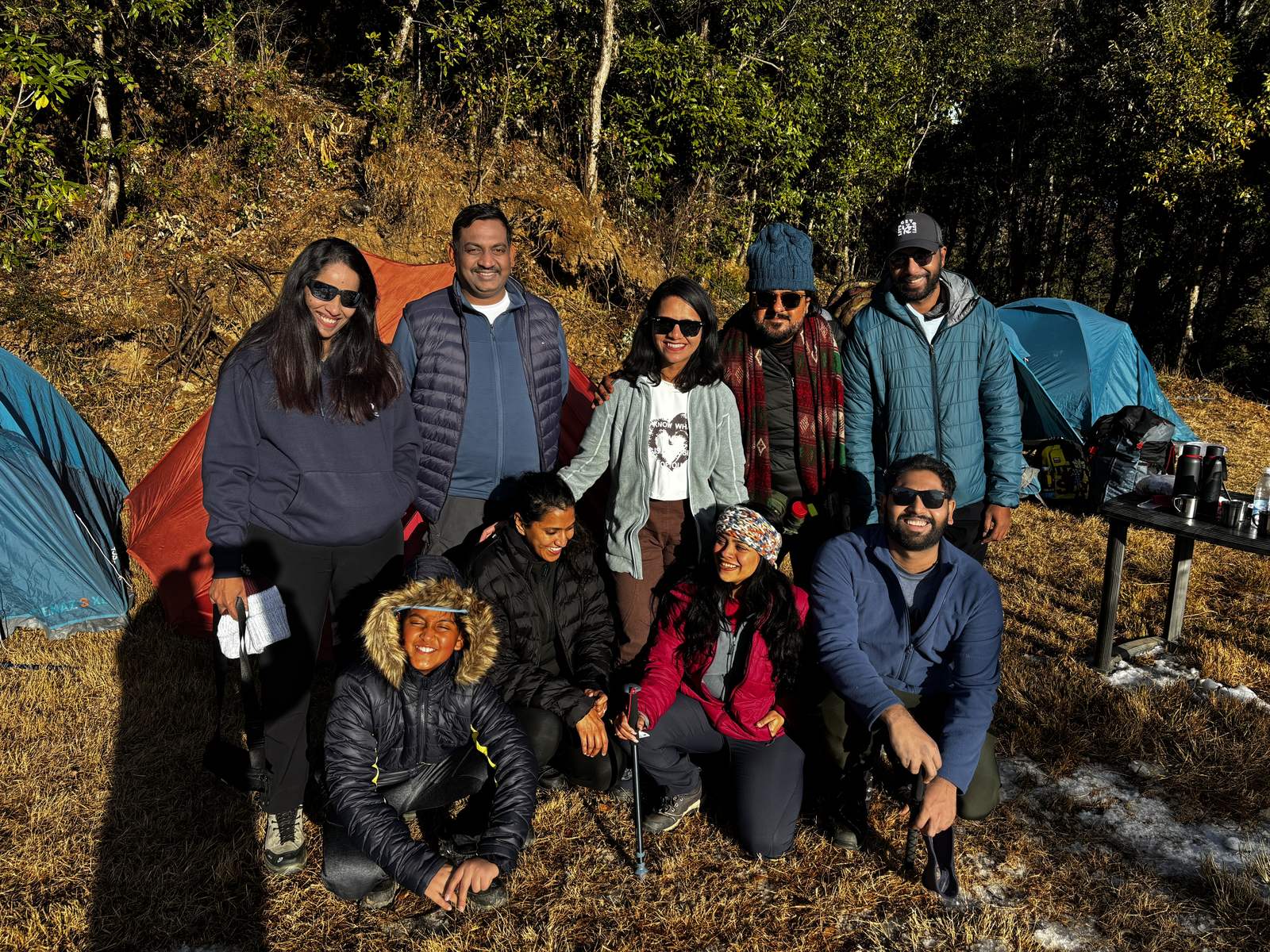 Trekkers posing at the Deoriatal campsite with tents behind in golden light