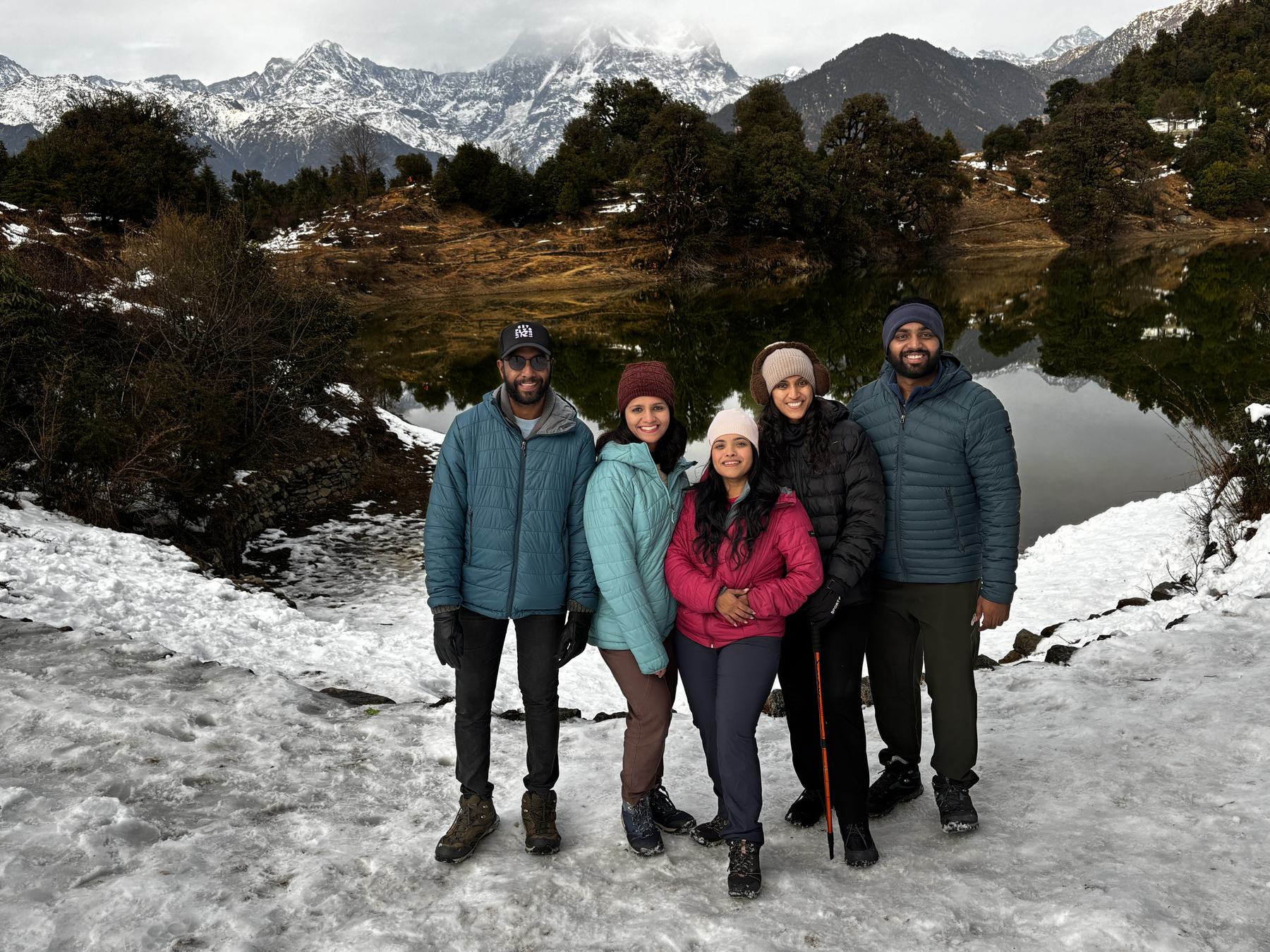 Trekkers standing on snow at Deoriatal lake with the Himalayan peaks behind