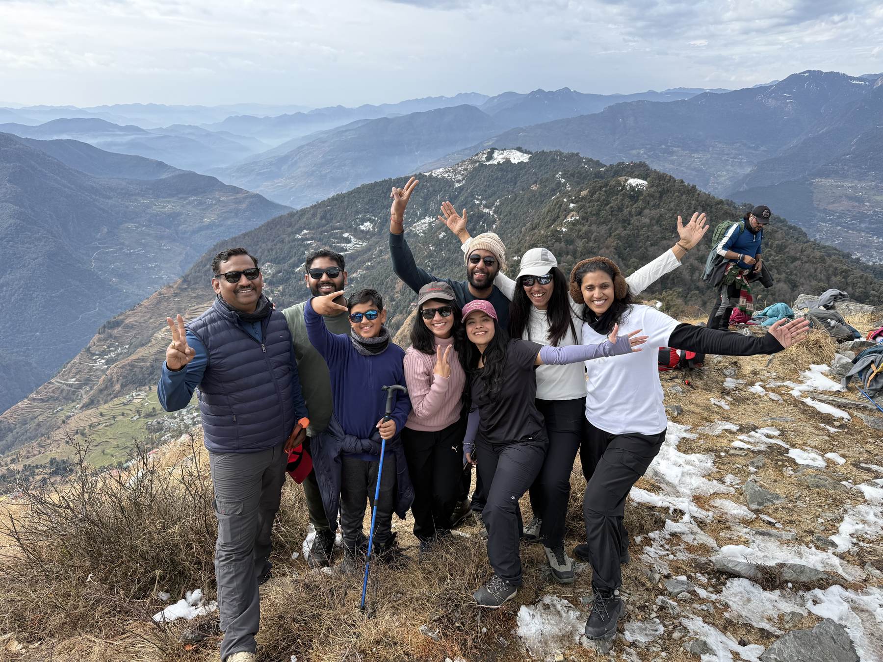 Trekkers posing on a ridge with patches of snow and a deep valley behind