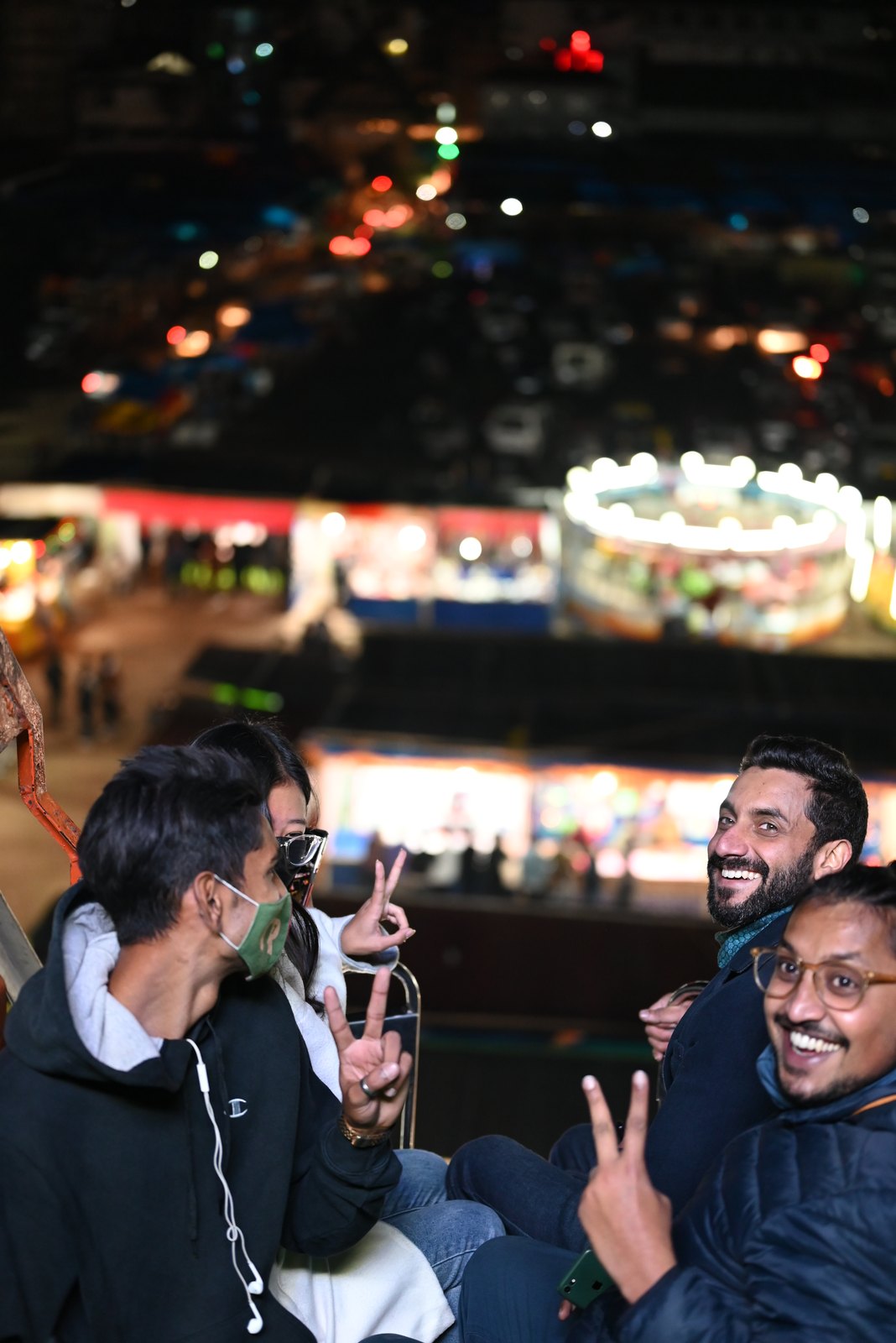 Friends on the giant wheel at the night carnival, flashing peace signs