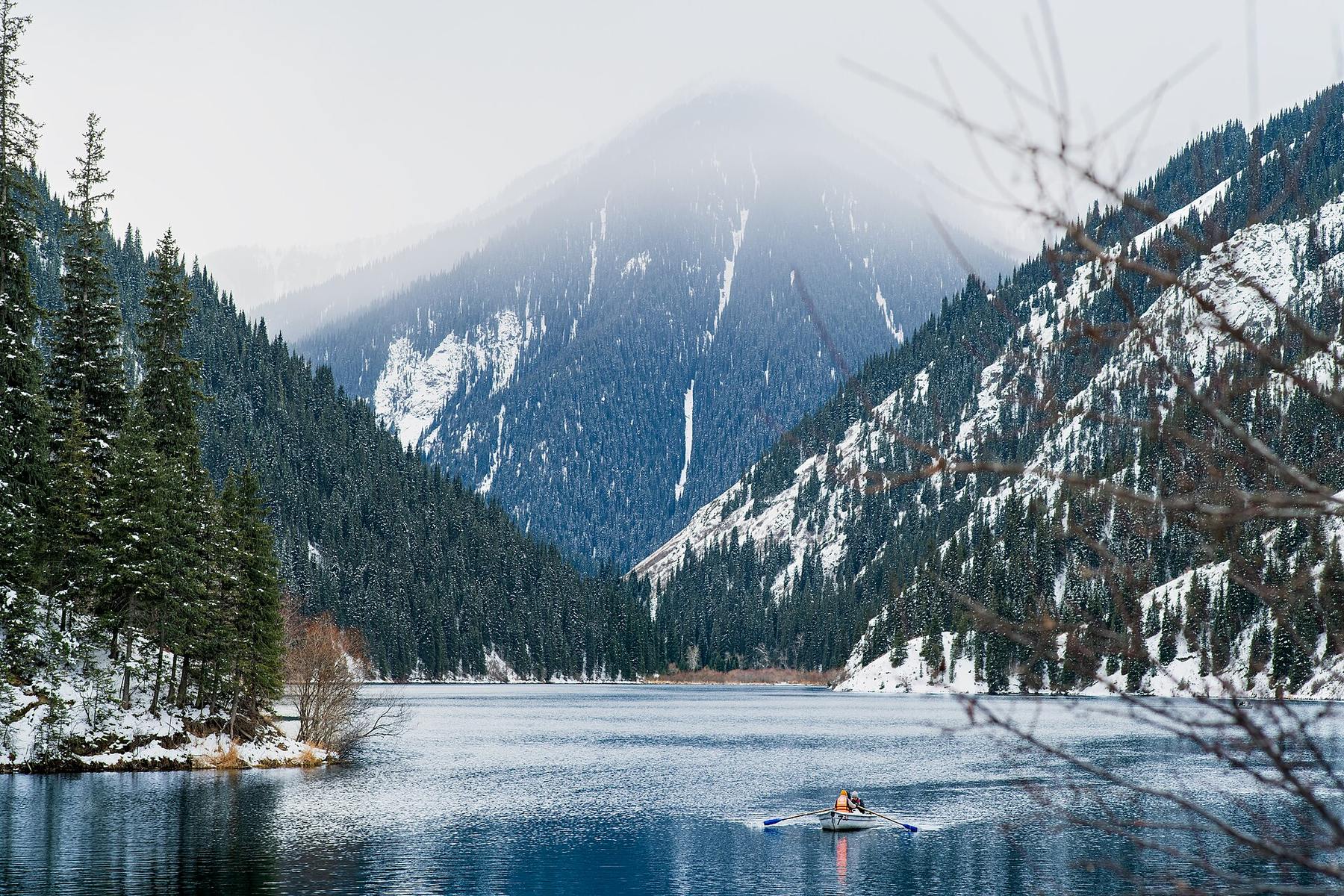Snow on the slopes above Kolsai Lake, with a single kayak on the water