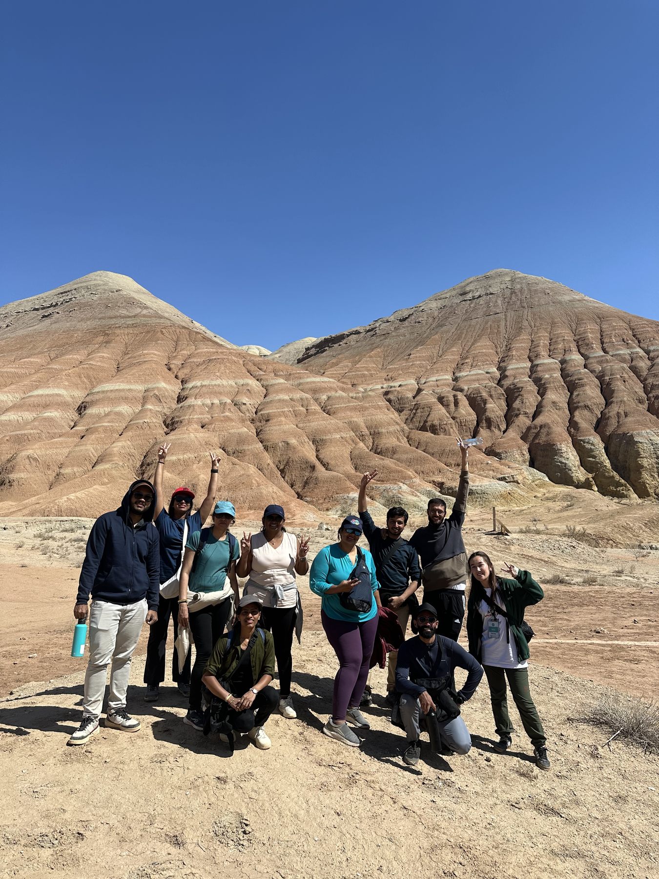 The crew with arms raised in front of the striped Aktau hills