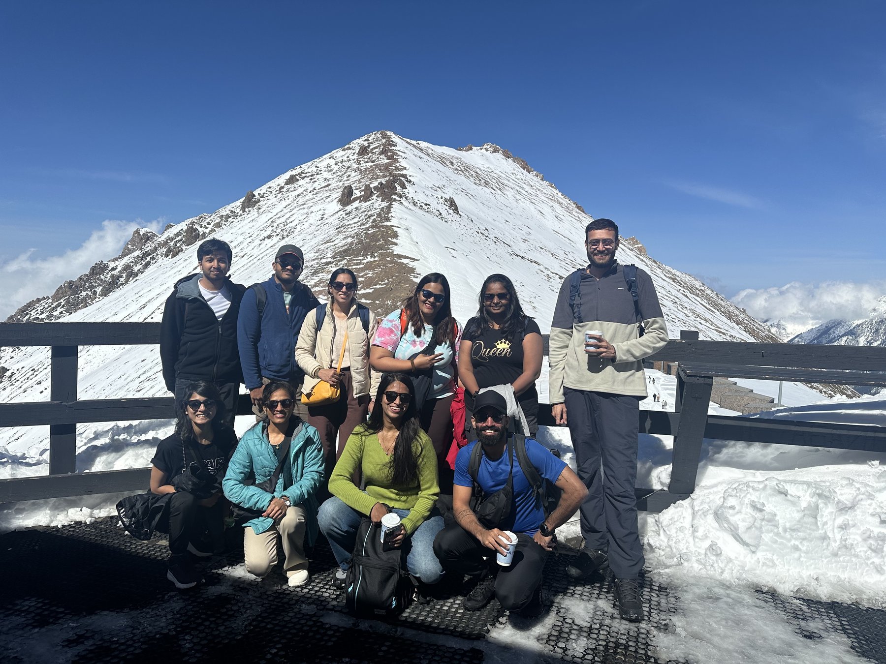 The crew on the snowy deck at Shymbulak with the white peak behind