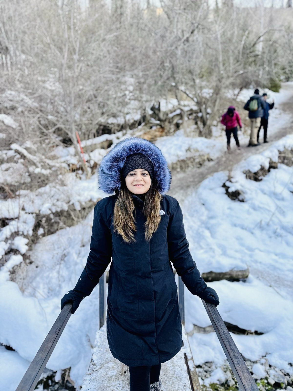 A tripper in a fur-hooded coat on a snowy forest trail, other trekkers on the path behind