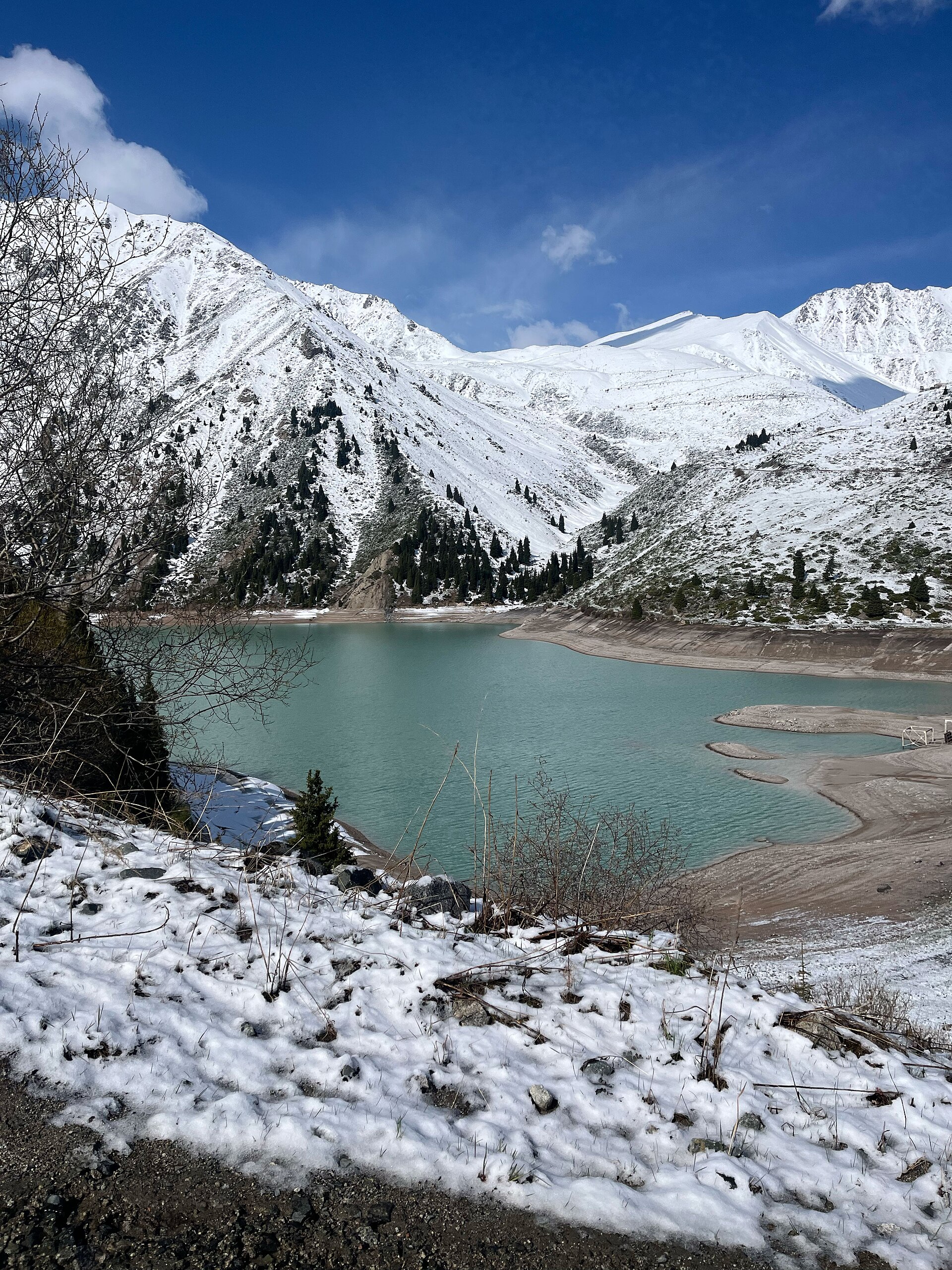 A frozen alpine lake in winter Kazakhstan, snow on the shore and snowy Tian Shan peaks behind
