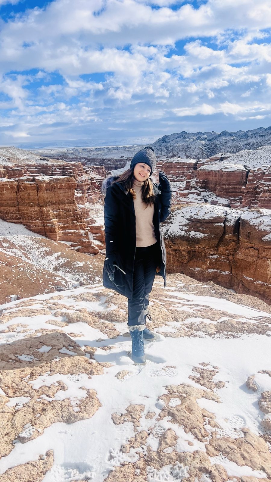 A tripper on a snow-dusted ledge at Charyn Canyon, red rock behind