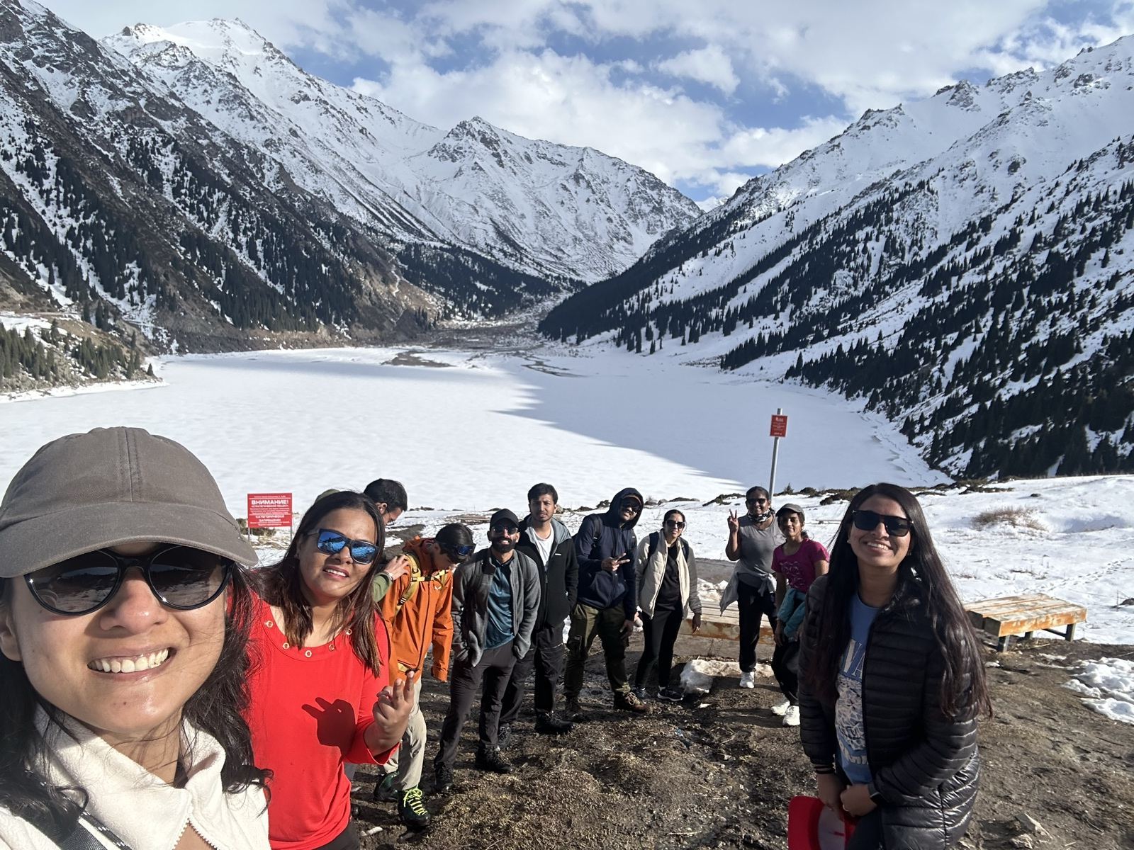 OJ group selfie at snow-covered Big Almaty Lake with the mountains behind