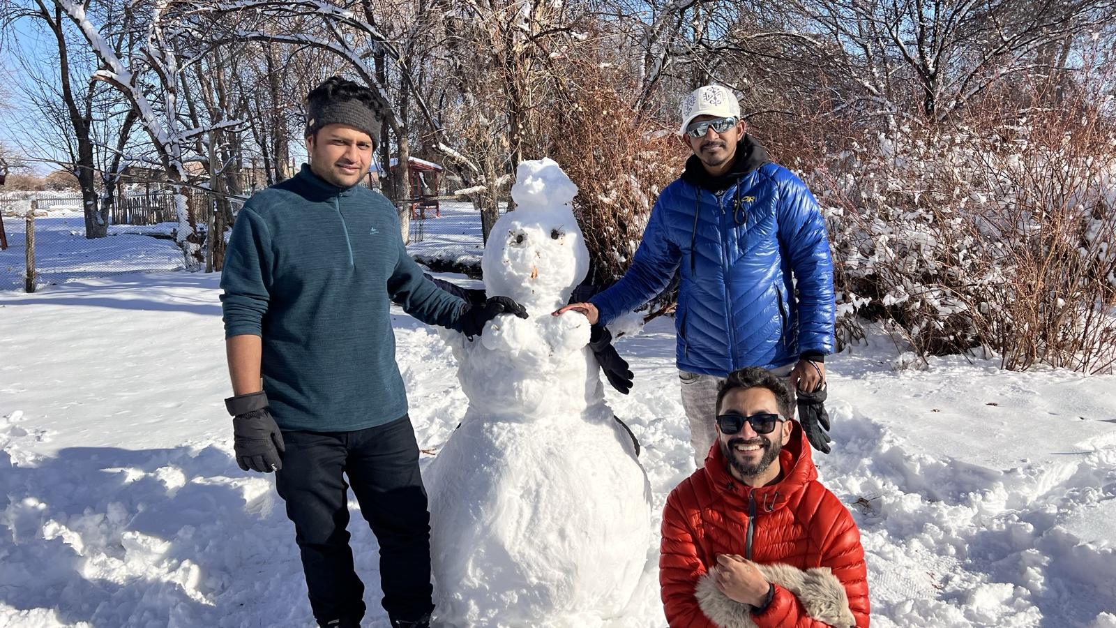 Three trippers posing with a snowman in a snowy park