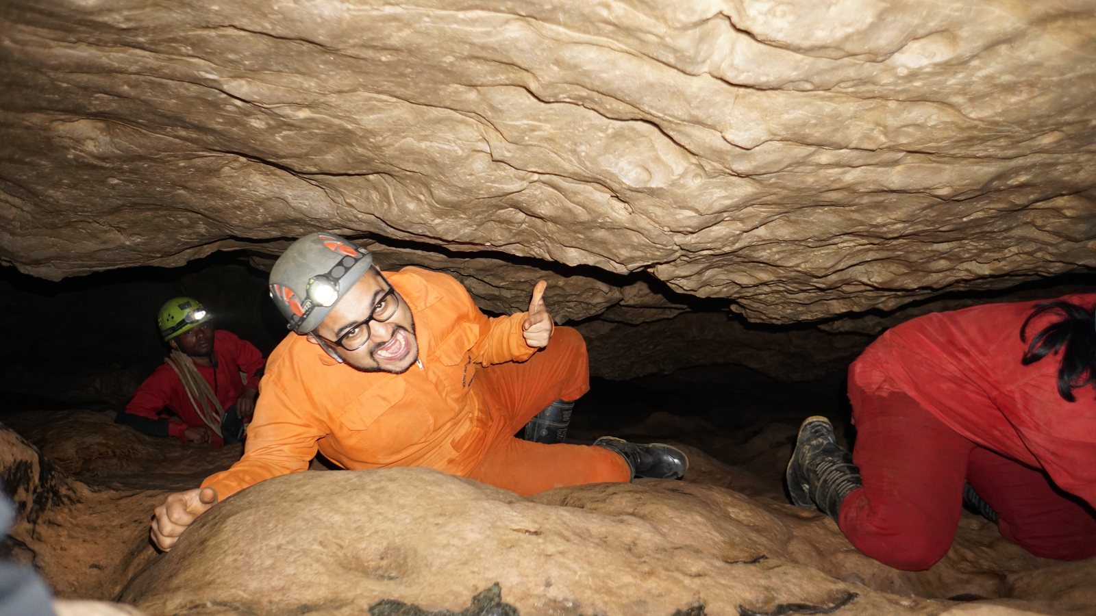 Meghalaya, Day 6, caving: tripper in an orange caving suit giving a thumbs up during a belly crawl