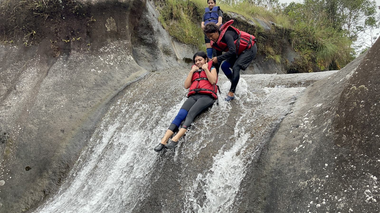 Meghalaya, Day 2, river canyoning: two trippers in life jackets sliding down a rock waterfall