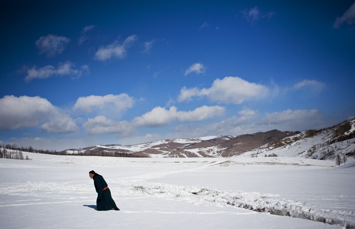 Herder walking across a snowy valley toward his ger