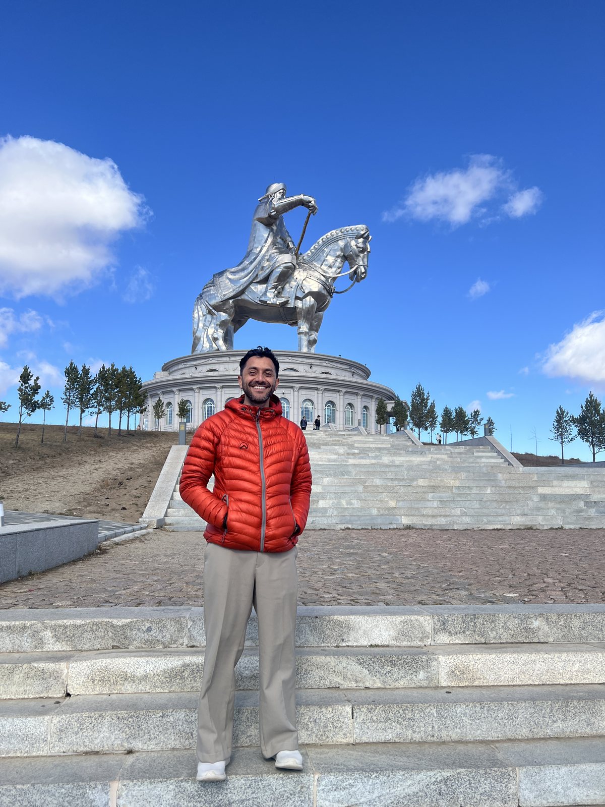 Tripper in an orange jacket at the foot of the Chinggis Khaan statue