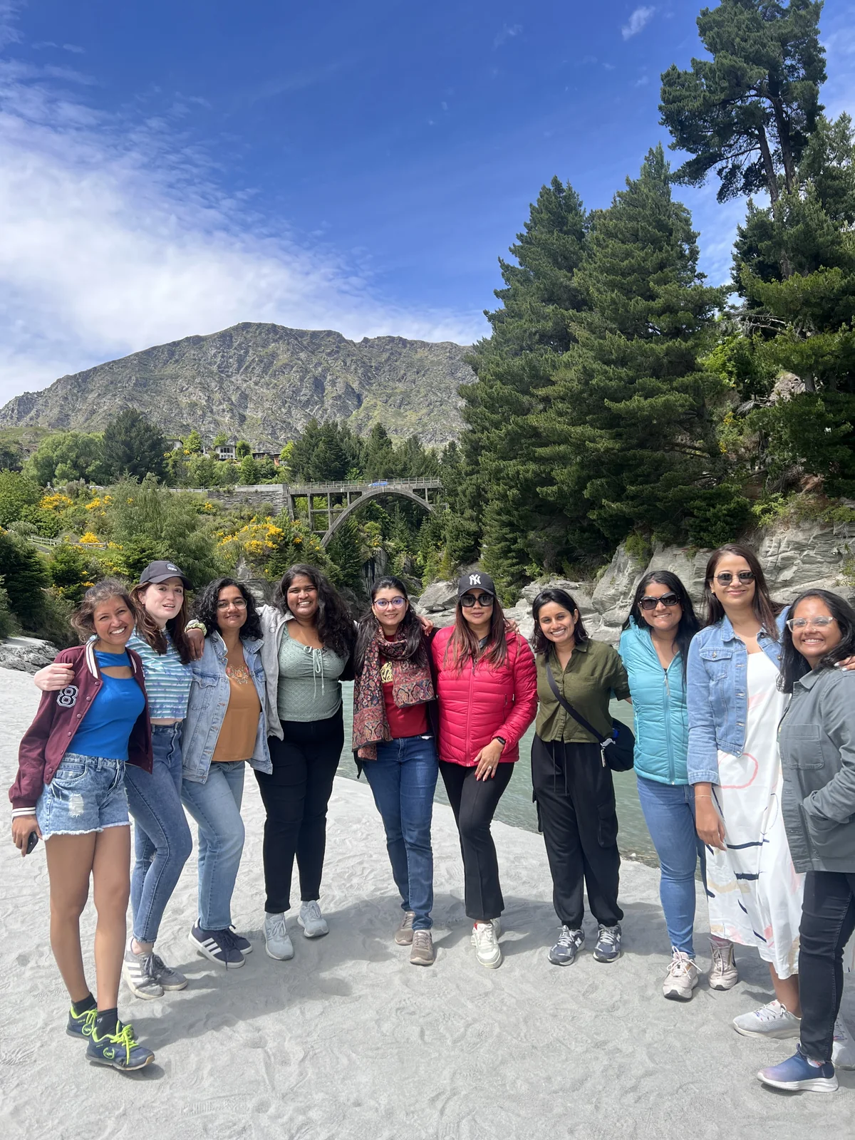 Ten OJ trippers in one group portrait on a riverbank with mountains behind