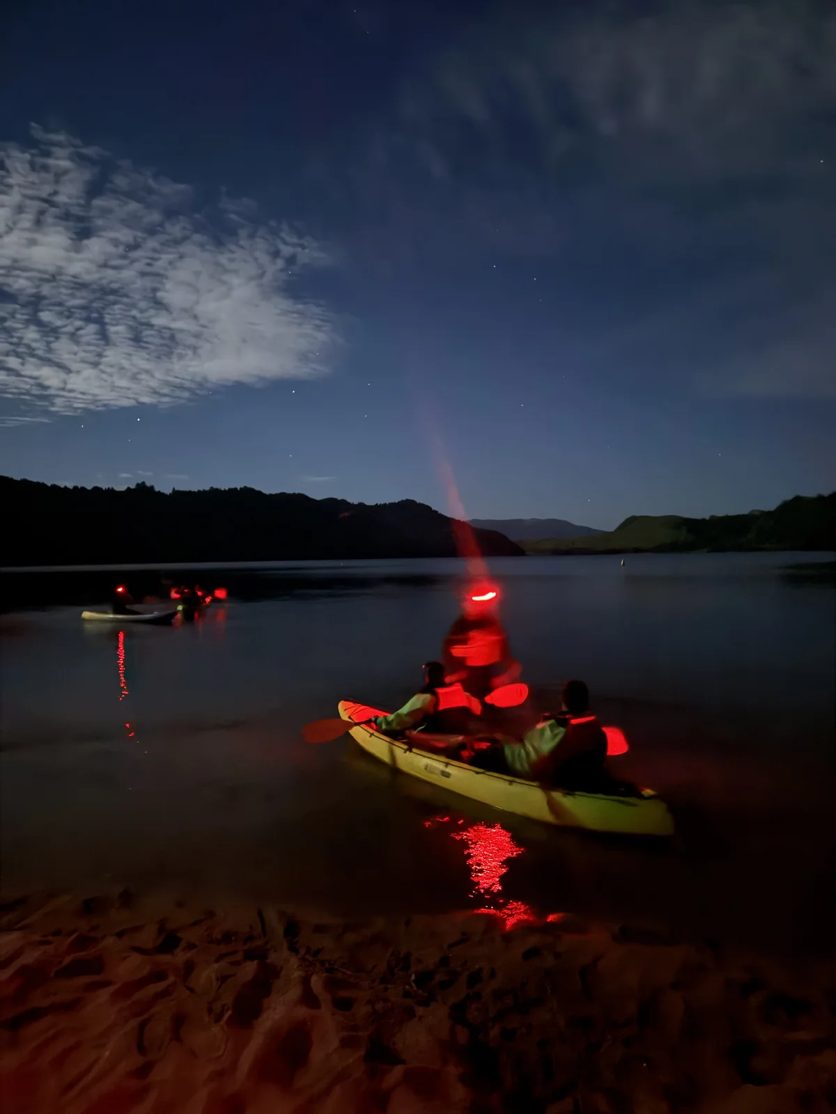 OJ kayakers on a dark Rotorua lake at night, red headlamps glowing on the water