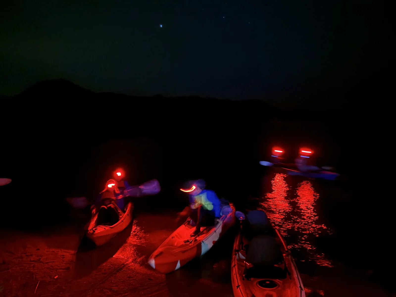 OJ kayakers with red headlamps launching onto a dark lake for the night glowworm kayak