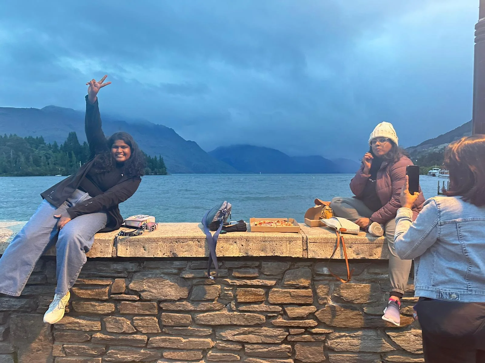 OJ trippers on the stone wall by Lake Wakatipu in Queenstown at blue hour, one waving at the camera