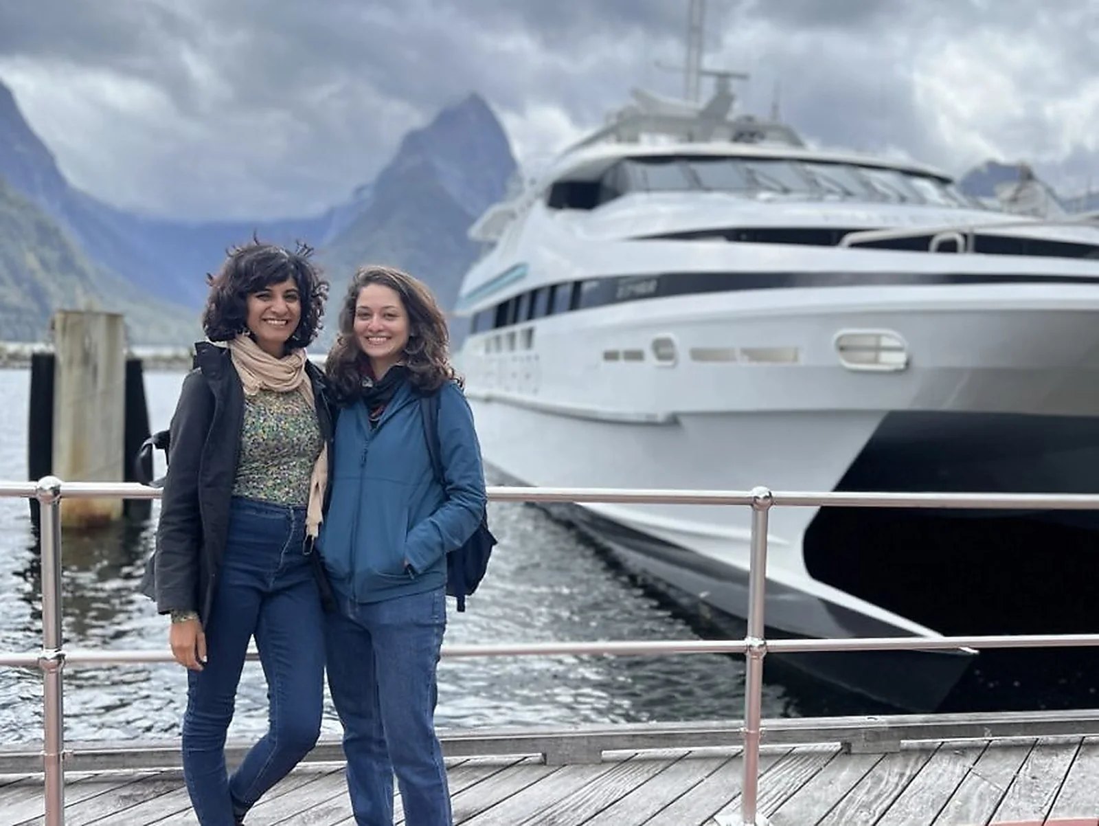 Two OJ trippers on the Milford Sound wharf with a cruise ship docked behind them