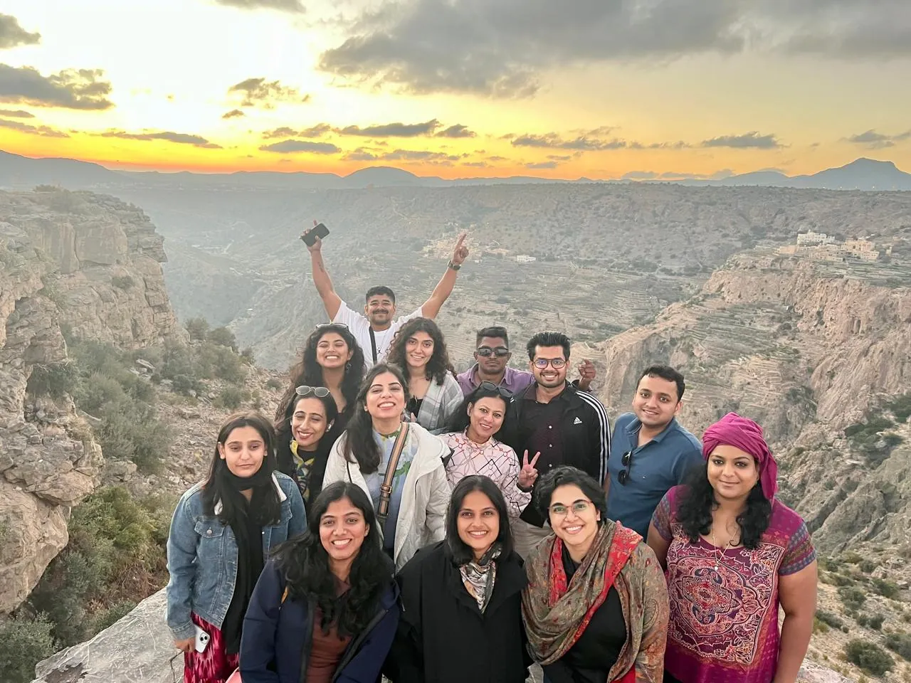 OJ crew on a mountain cliff edge at sunset, arms raised