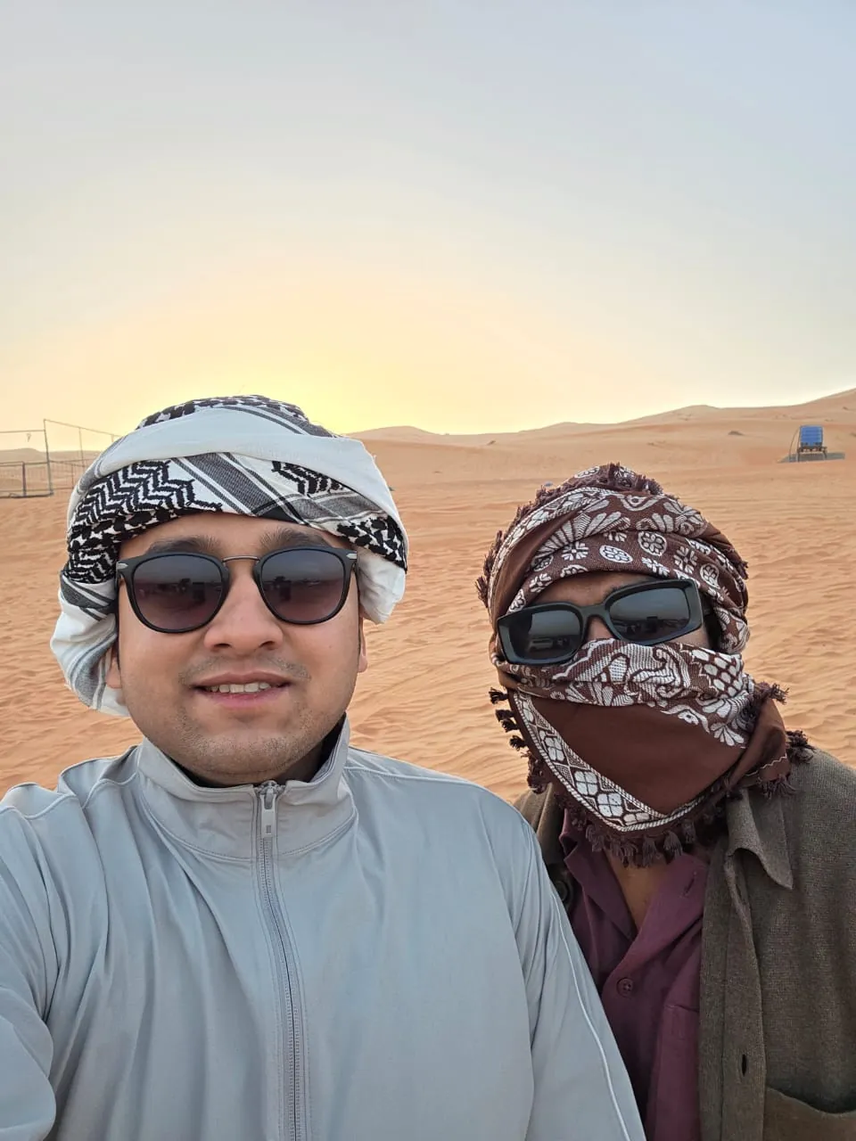 Two OJ trippers in keffiyehs among the desert dunes at sunset