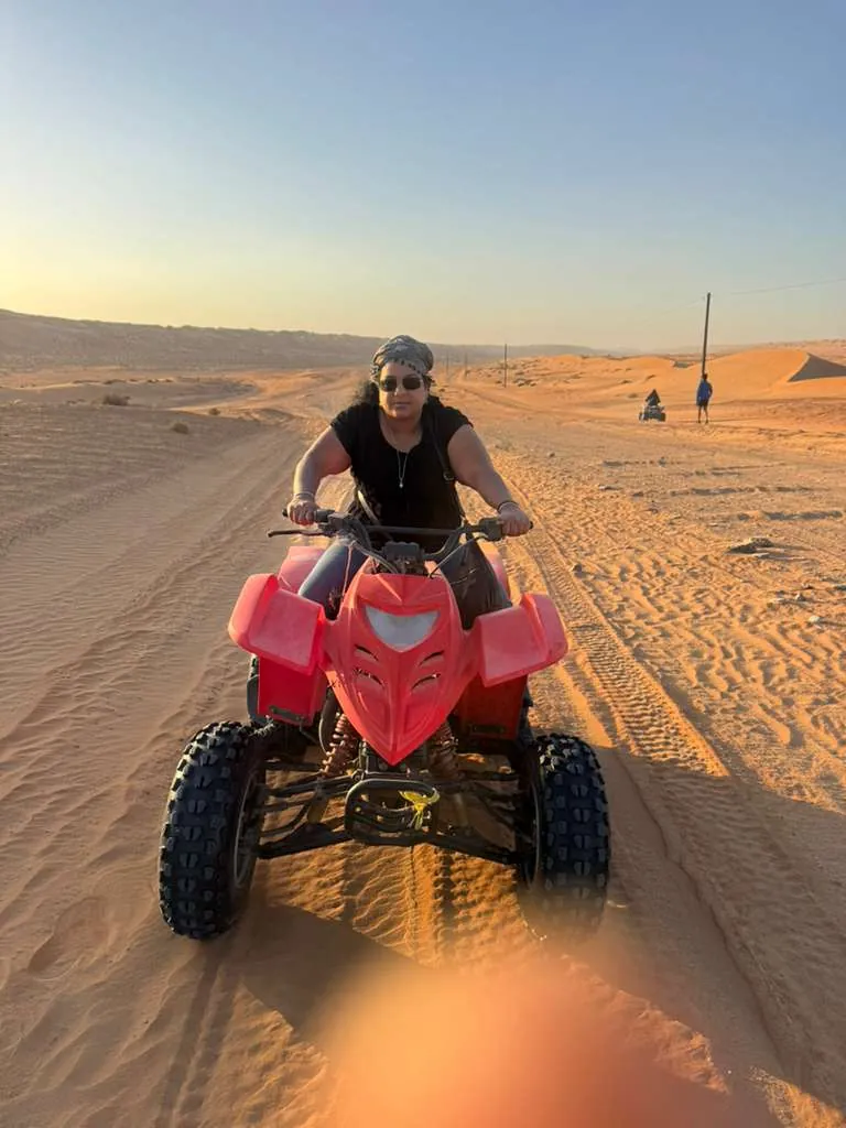 An OJ tripper riding a red quad bike across the desert dunes