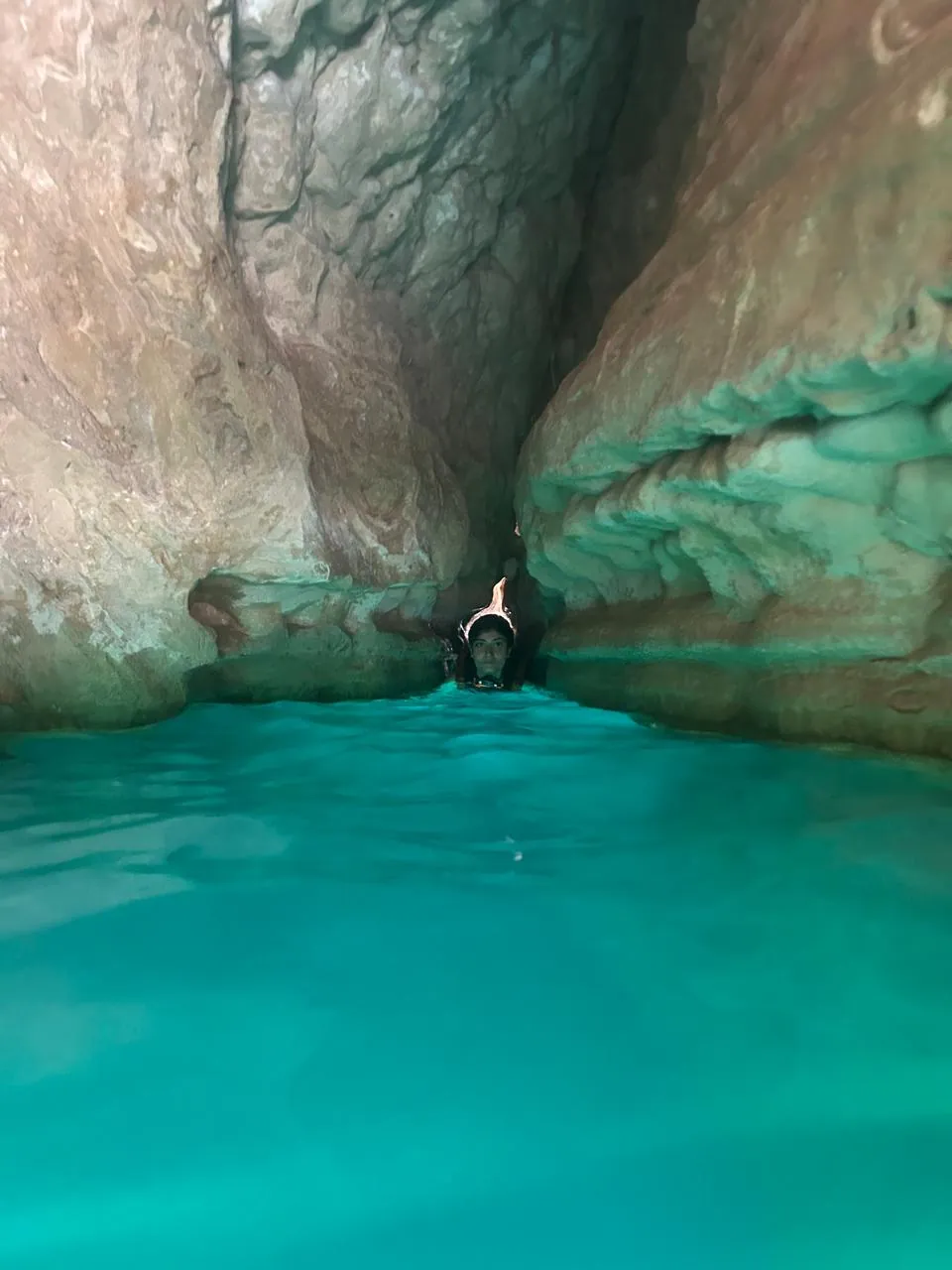 An OJ tripper swimming into a narrow turquoise cave gap in the canyon