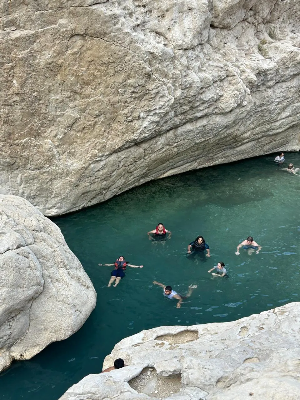 The OJ crew floating in a turquoise pool beneath white limestone
