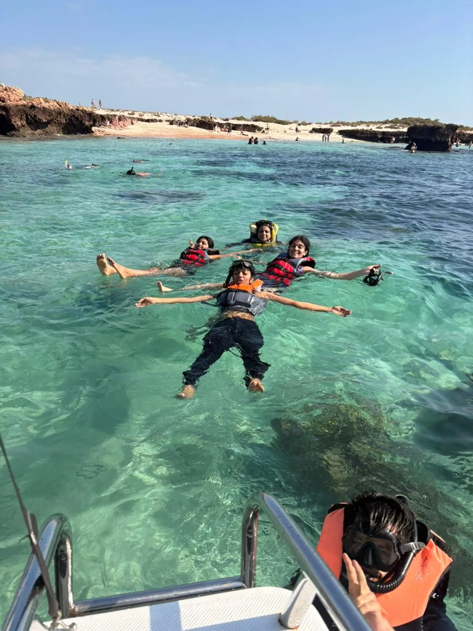 The OJ crew floating in life vests in clear turquoise water off a white-sand island